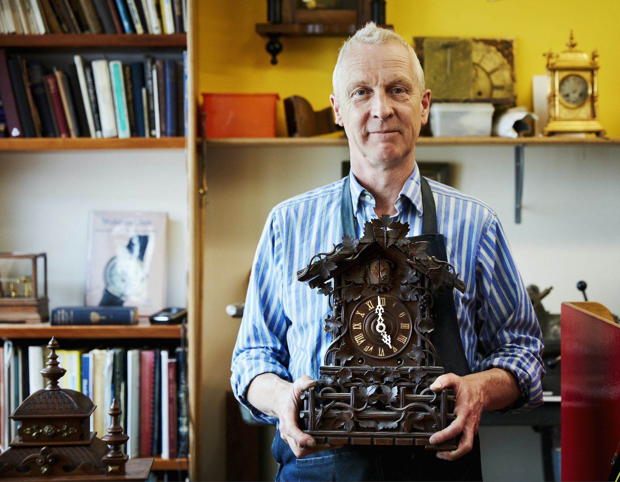 A clock maker and repairer holding an antique cuckoo clock.